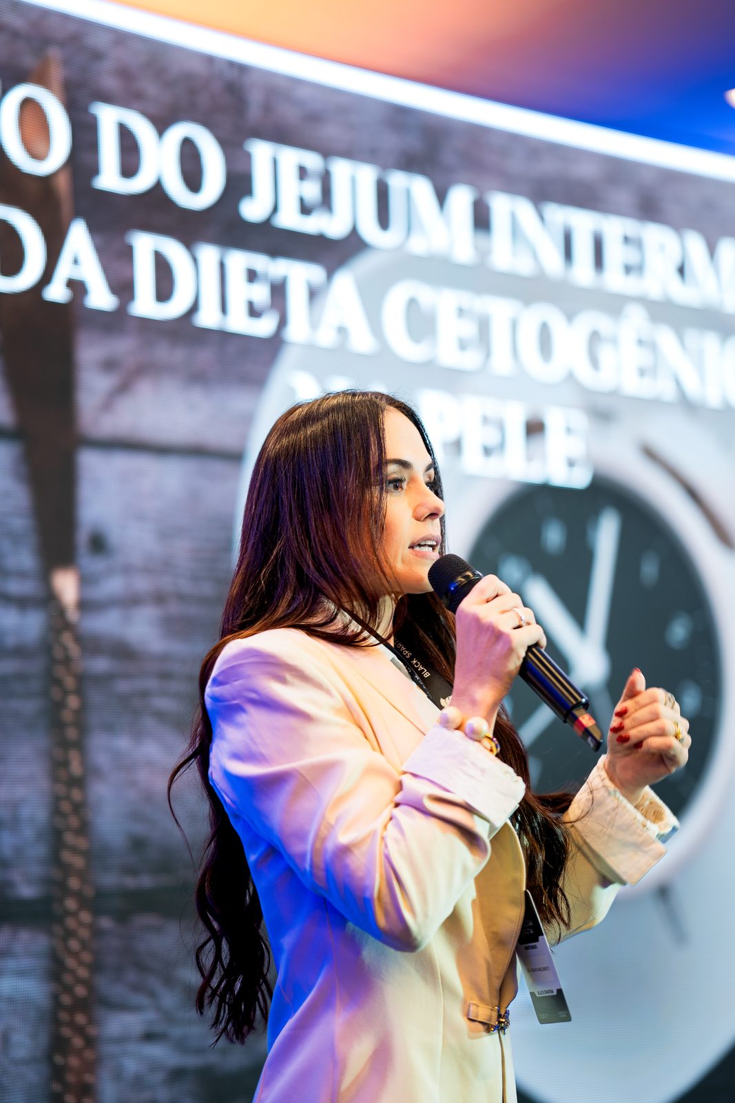 Dra. Renata Nascimento palestrando com microfone sobre saúde metabólica feminina, com telão ao fundo